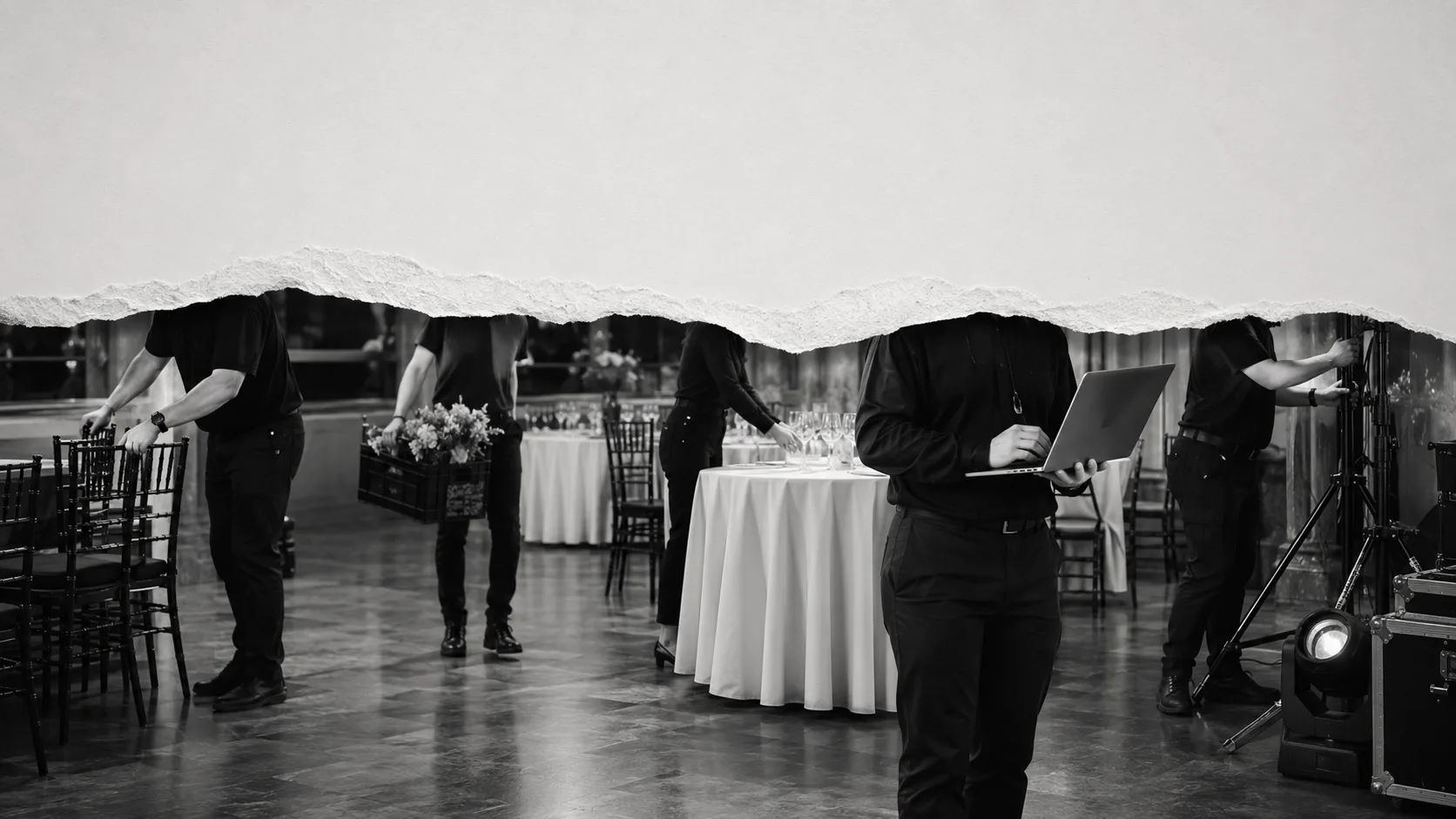 A black-and-white event floor mid-service — tables dressed, staff at their stations, every head torn out of the frame